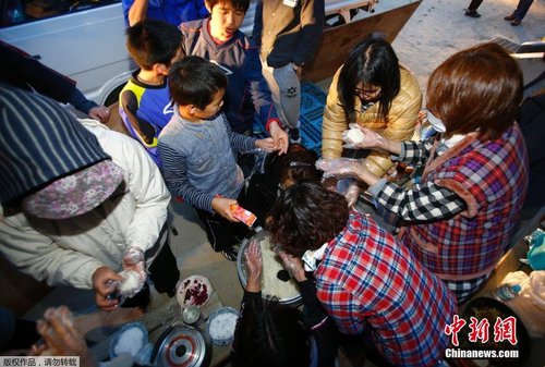 當地時間4月17日，志愿者在公園的空地上制作飯團發放給小朋友。